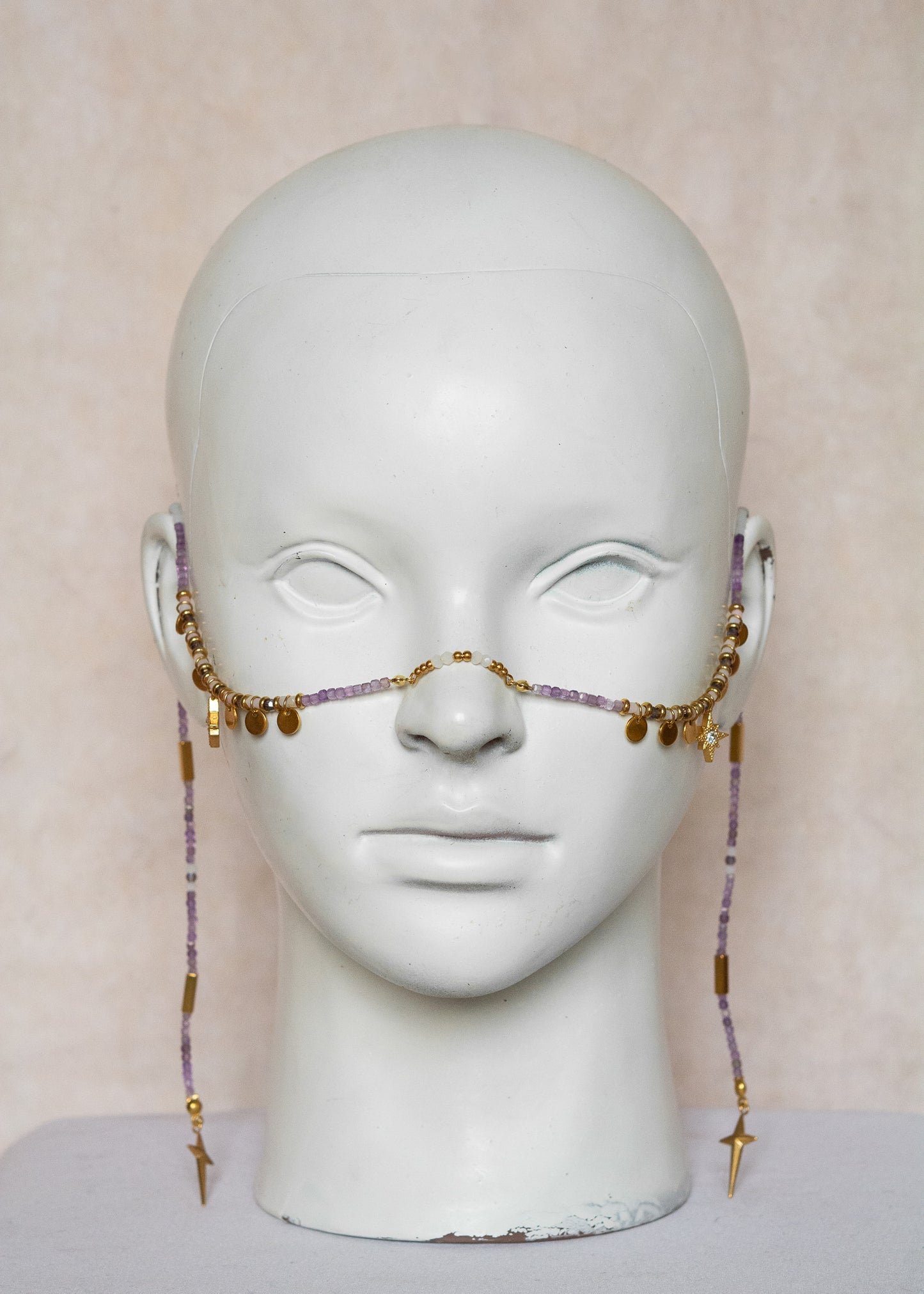 Chaîne de visage avec pierres naturelles d’améthyste et éléments en acier inoxydable doré | Croix stylisées aux extrémités, étoiles dorées et strass translucides sur les joues | Accessoire facial artisanal fait main à Montréal | Bijou de tête pour festival, costume ou tenue artistique | Idéal pour scène, spectacle ou événement spécial.