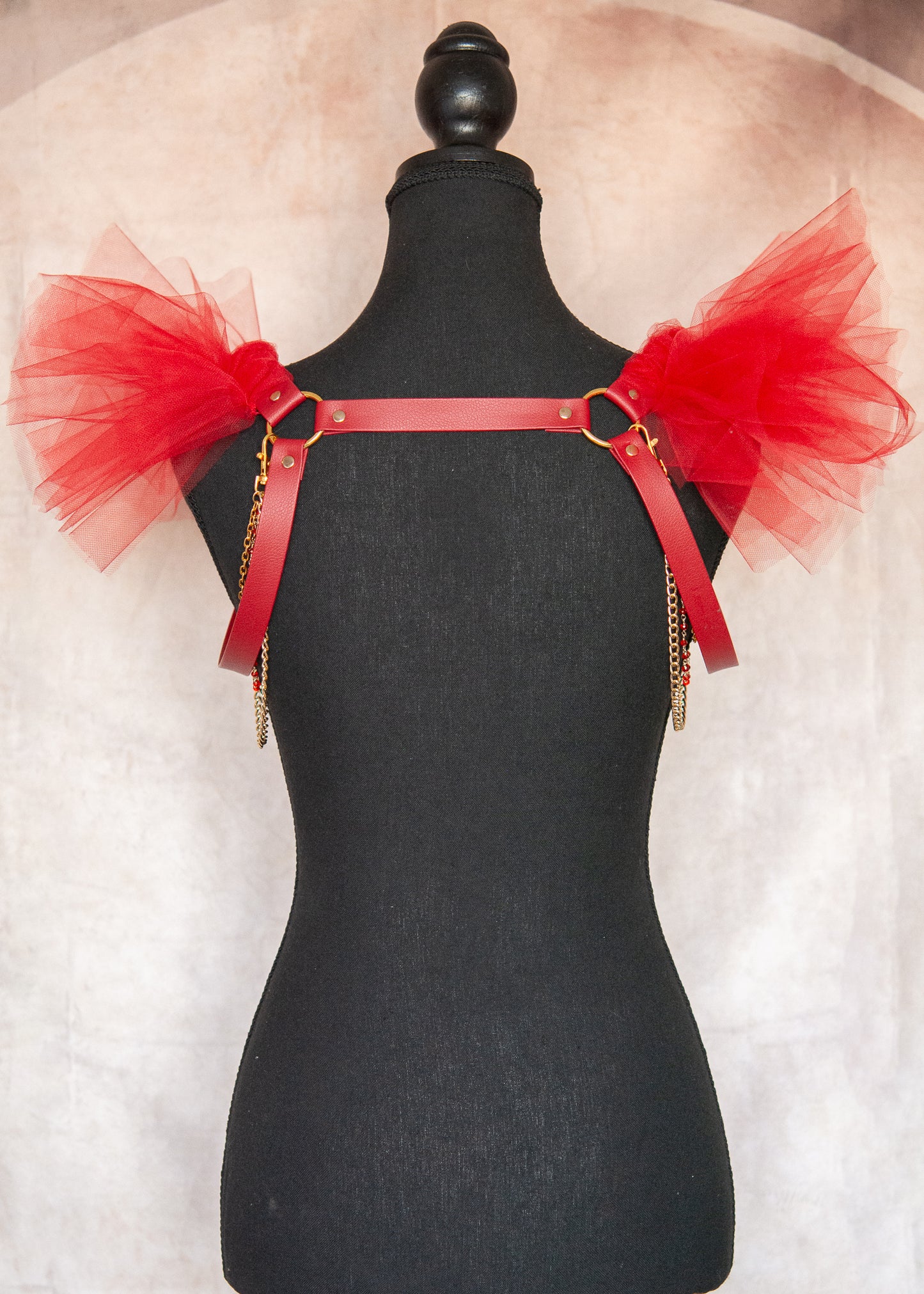 Harnais d'épaules audacieux en vinyle rouge végane avec épaulettes aériennes en tulle rouge et chaînes dorées amovibles. Cette pièce statement transforme instantanément votre silhouette en une célébration de force et de mystère, parfaite pour les festivals, soirées ou pour réinventer vos tenues quotidiennes avec une touche de magie guerrière.