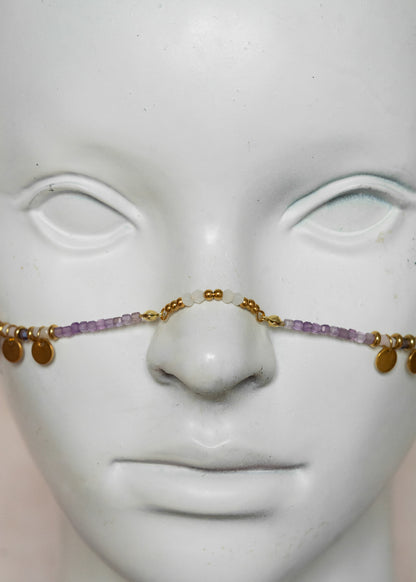 Chaîne de visage avec pierres naturelles d’améthyste et éléments en acier inoxydable doré | Croix stylisées aux extrémités, étoiles dorées et strass translucides sur les joues | Accessoire facial artisanal fait main à Montréal | Bijou de tête pour festival, costume ou tenue artistique | Idéal pour scène, spectacle ou événement spécial.