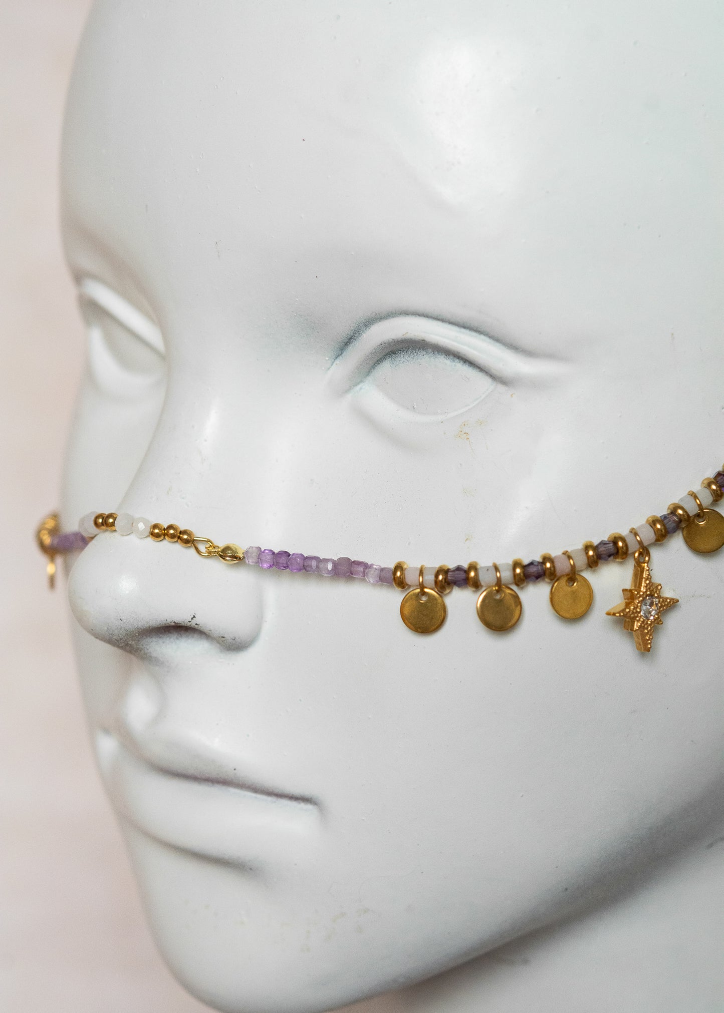 Chaîne de visage avec pierres naturelles d’améthyste et éléments en acier inoxydable doré | Croix stylisées aux extrémités, étoiles dorées et strass translucides sur les joues | Accessoire facial artisanal fait main à Montréal | Bijou de tête pour festival, costume ou tenue artistique | Idéal pour scène, spectacle ou événement spécial.