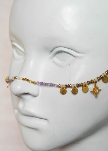 Chaîne de visage avec pierres naturelles d’améthyste et éléments en acier inoxydable doré | Croix stylisées aux extrémités, étoiles dorées et strass translucides sur les joues | Accessoire facial artisanal fait main à Montréal | Bijou de tête pour festival, costume ou tenue artistique | Idéal pour scène, spectacle ou événement spécial.