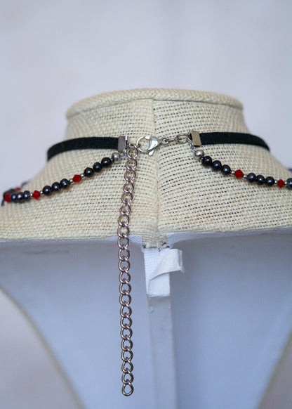 Choker en suède noir avec perles d'eau douce teintées en noir nacré, cristaux rouges et croix. Bijou vampirique goth élégant, inspiré d’une trinité obscure.