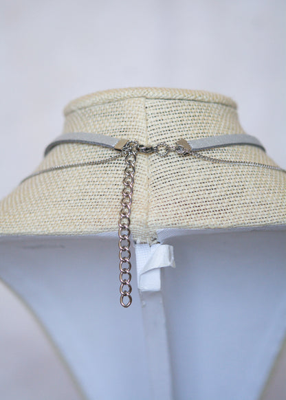 Collier en suède argenté avec soleil émaillé blanc, strass et détails en acier. Bijou léger d’inspiration céleste et angélique.