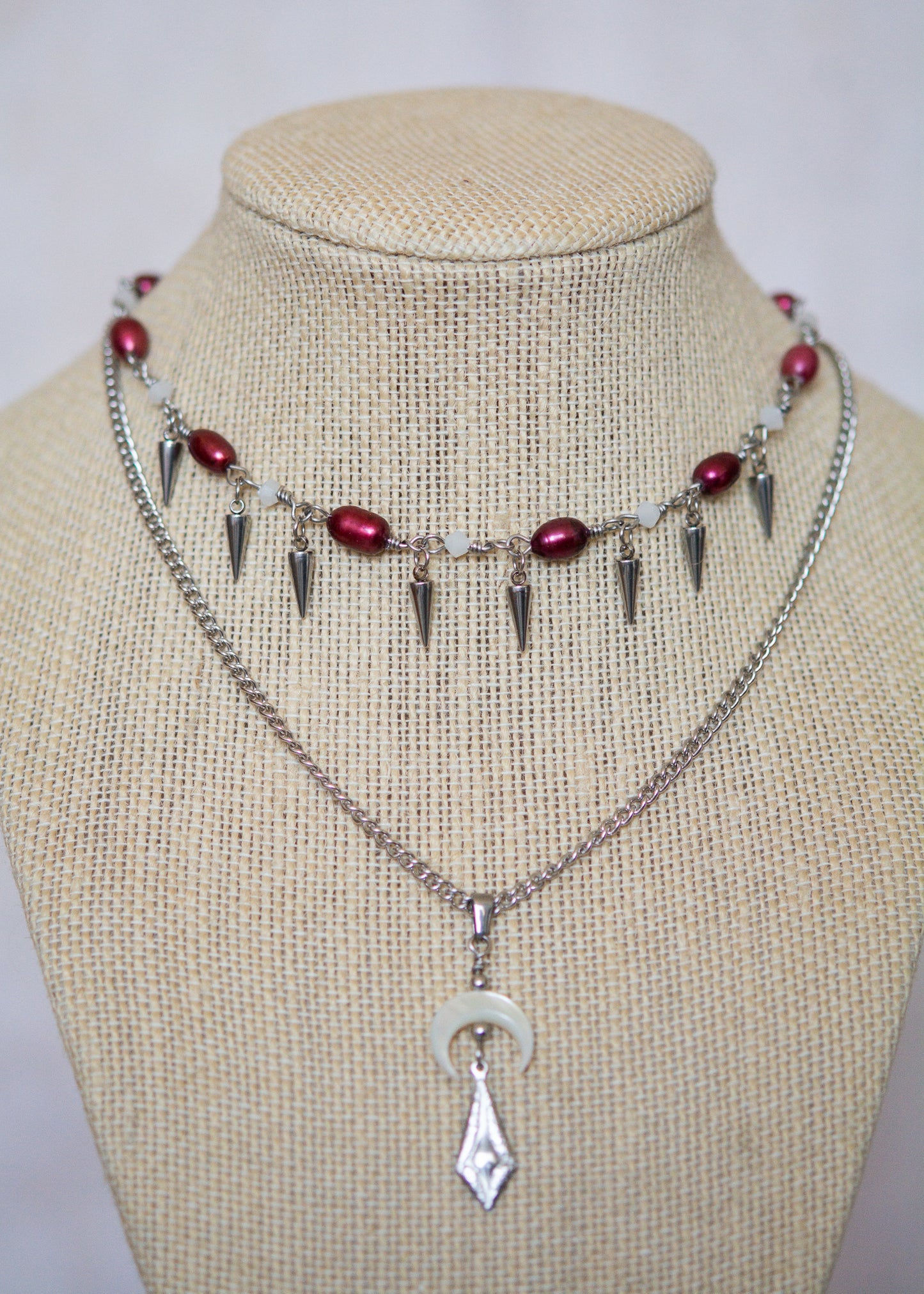 Collier en acier avec perles d'eau douce teintées rouge sang, piques, lune nacrée et charme mystique. Bijou rituel gothique, puissant et ensorcelant.