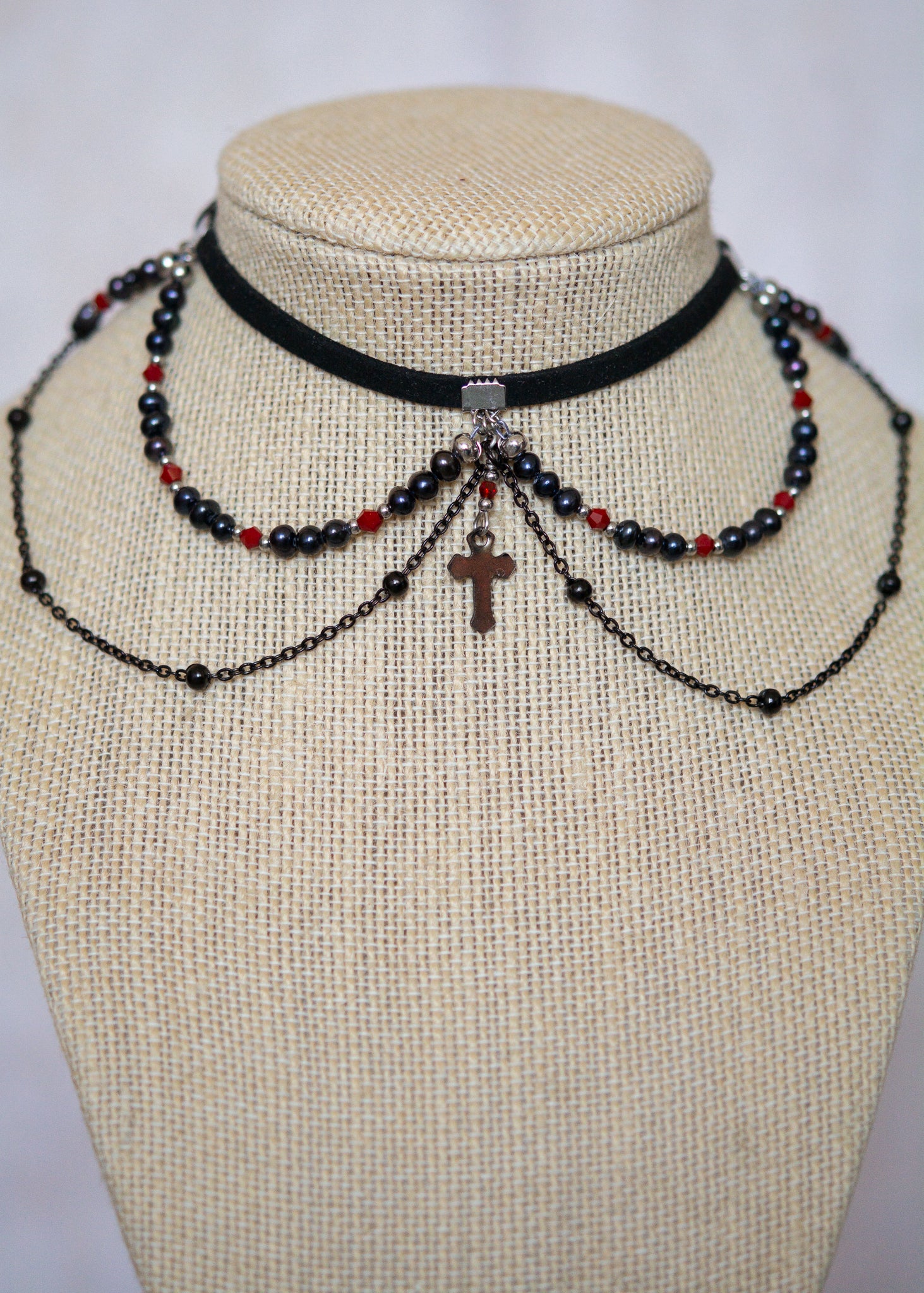 Choker en suède noir avec perles d'eau douce teintées en noir nacré, cristaux rouges et croix. Bijou vampirique goth élégant, inspiré d’une trinité obscure.