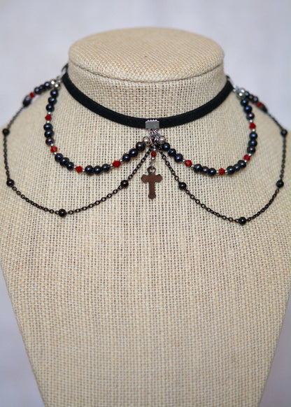 Choker en suède noir avec perles d'eau douce teintées en noir nacré, cristaux rouges et croix. Bijou vampirique goth élégant, inspiré d’une trinité obscure.