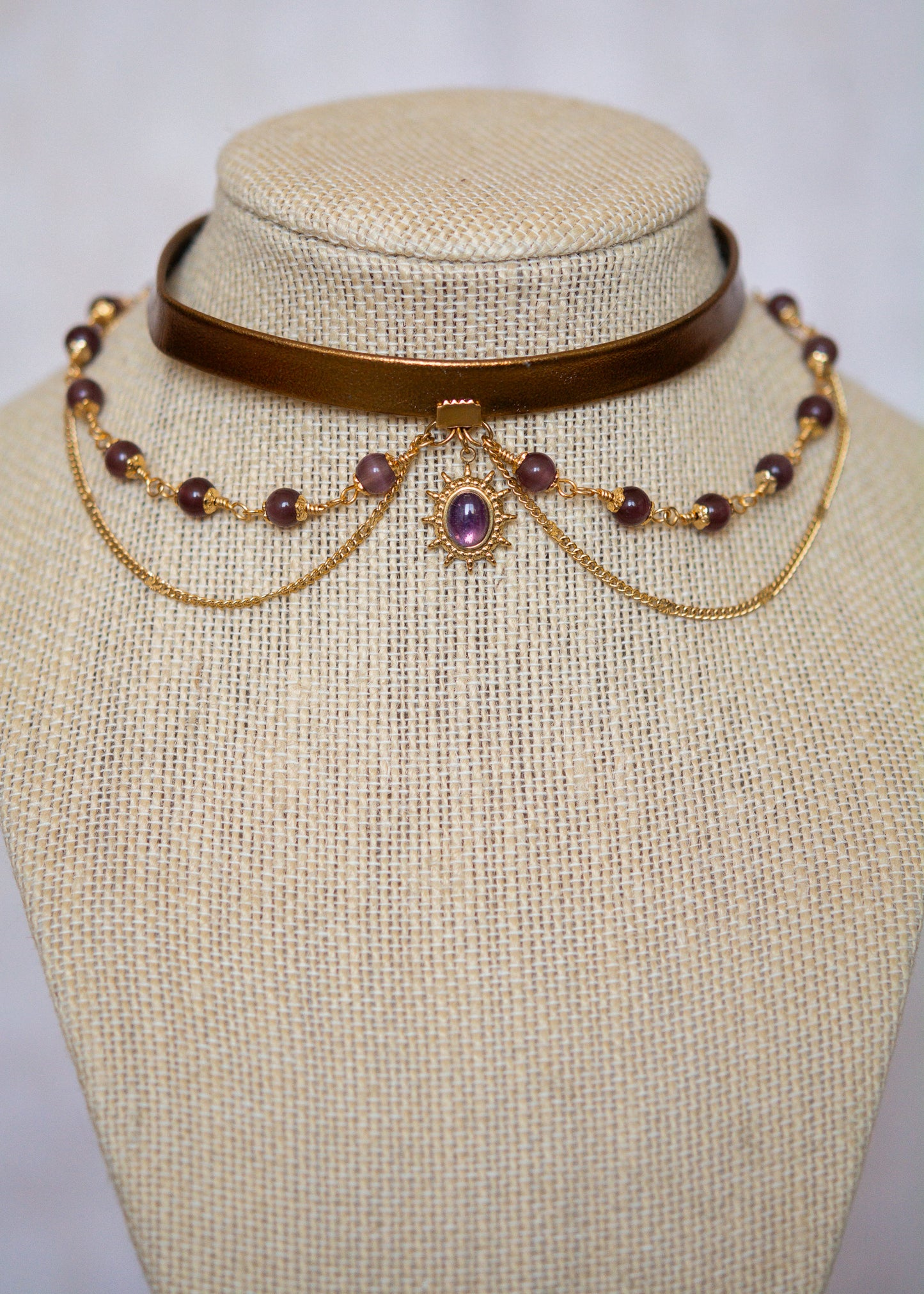 Tour de cou en cuir doré avec soleil mystique, améthyste et perles œil de chat. Bijou oraculaire d’inspiration antique et ésotérique.