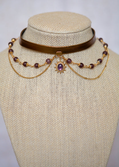 Tour de cou en cuir doré avec soleil mystique, améthyste et perles œil de chat. Bijou oraculaire d’inspiration antique et ésotérique.