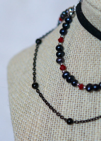Choker en suède noir avec perles d'eau douce teintées en noir nacré, cristaux rouges et croix. Bijou vampirique goth élégant, inspiré d’une trinité obscure.