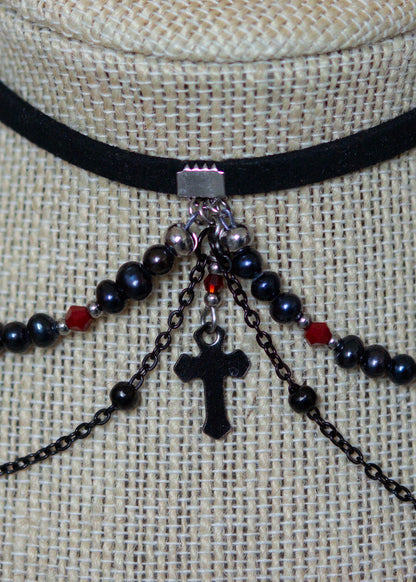 Choker en suède noir avec perles d'eau douce teintées en noir nacré, cristaux rouges et croix. Bijou vampirique goth élégant, inspiré d’une trinité obscure.
