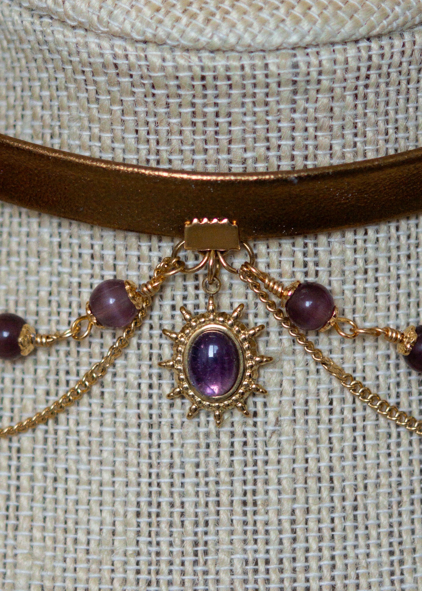 Tour de cou en cuir doré avec soleil mystique, améthyste et perles œil de chat. Bijou oraculaire d’inspiration antique et ésotérique.