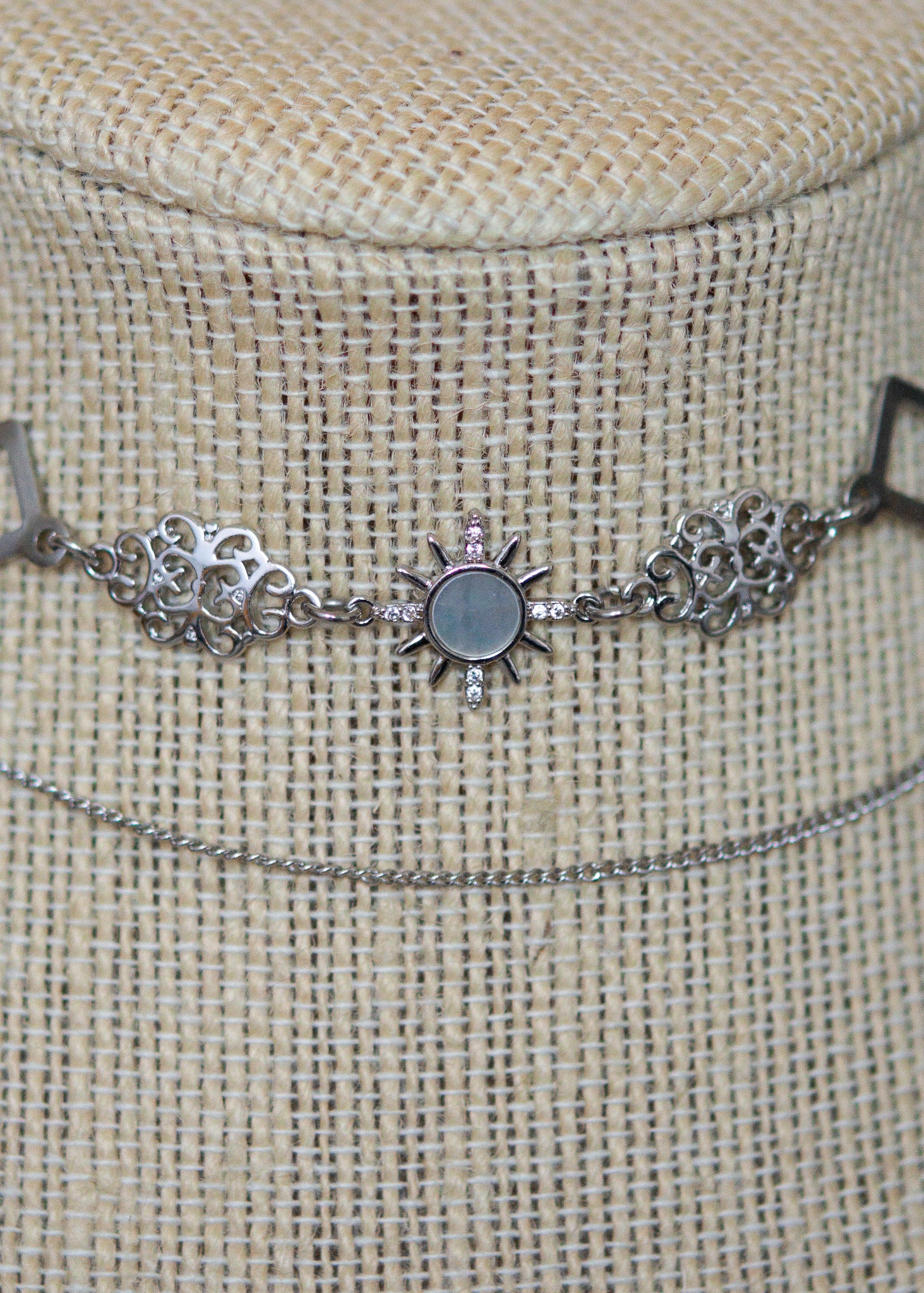 Collier en suède argenté avec soleil émaillé blanc, strass et détails en acier. Bijou léger d’inspiration céleste et angélique.
