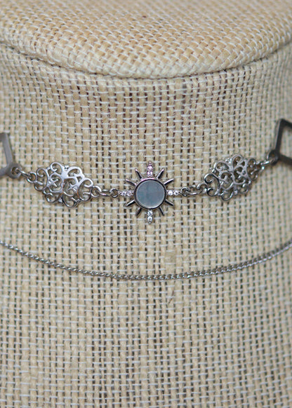 Collier en suède argenté avec soleil émaillé blanc, strass et détails en acier. Bijou léger d’inspiration céleste et angélique.