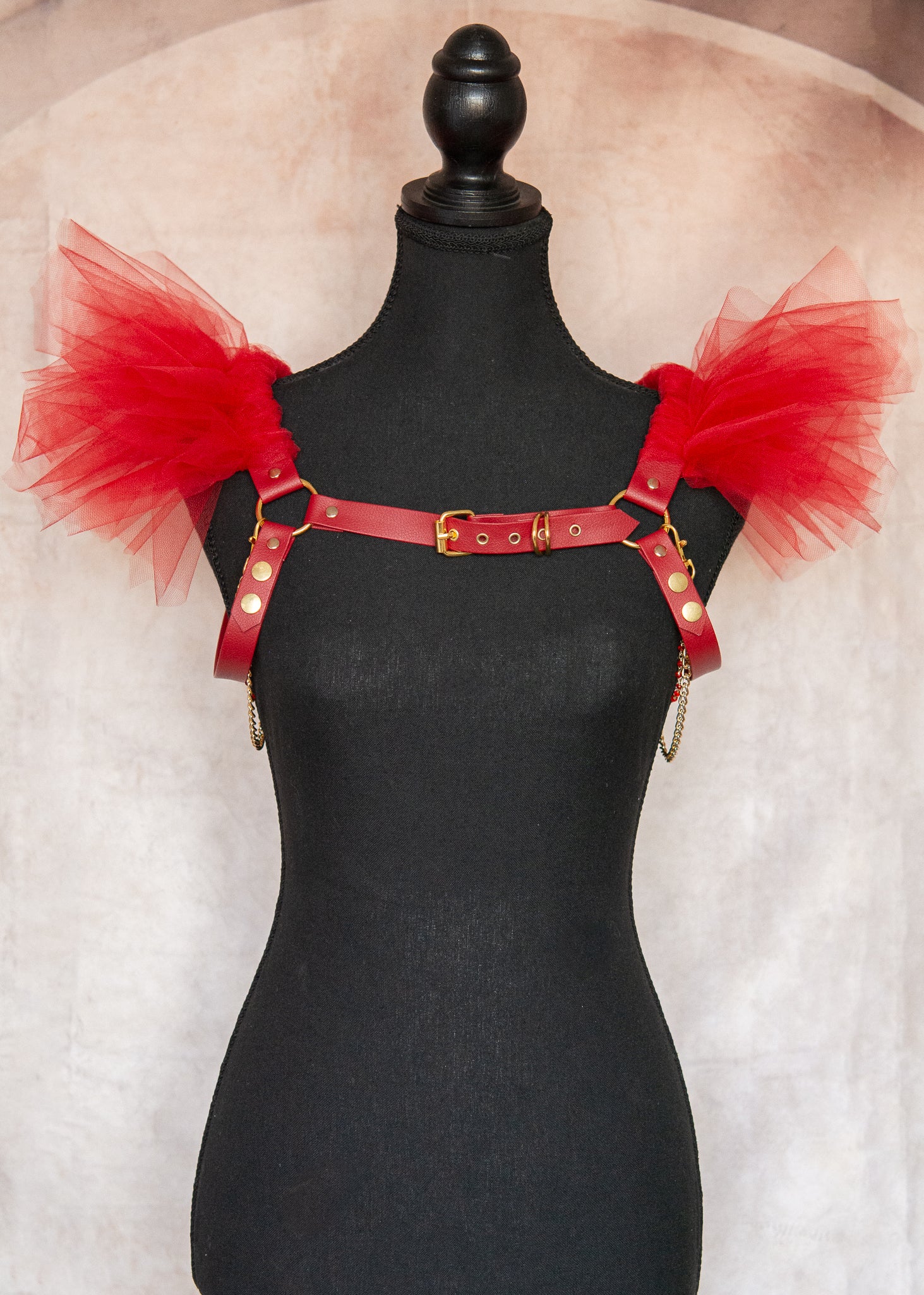 Harnais d'épaules audacieux en vinyle rouge végane avec épaulettes aériennes en tulle rouge et chaînes dorées amovibles. Cette pièce statement transforme instantanément votre silhouette en une célébration de force et de mystère, parfaite pour les festivals, soirées ou pour réinventer vos tenues quotidiennes avec une touche de magie guerrière.