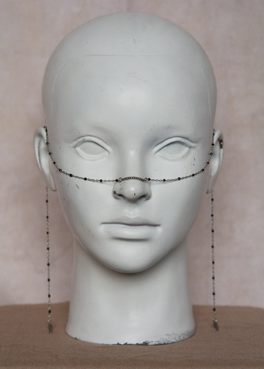 Bijou facial en chaîne fine avec perles d’émail noir et piques. Accessoire sombre et délicat pour look alternatif minimaliste.