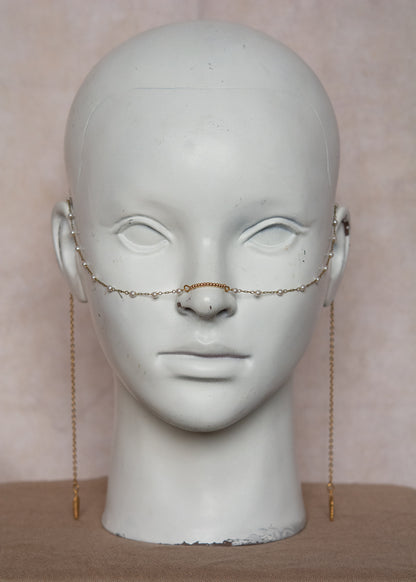 Bijou facial en chaîne d'acier inoxydable plaqué or avec perles synthétiques et plumes dorées. Accessoire léger et aérien, style boho, look festival.