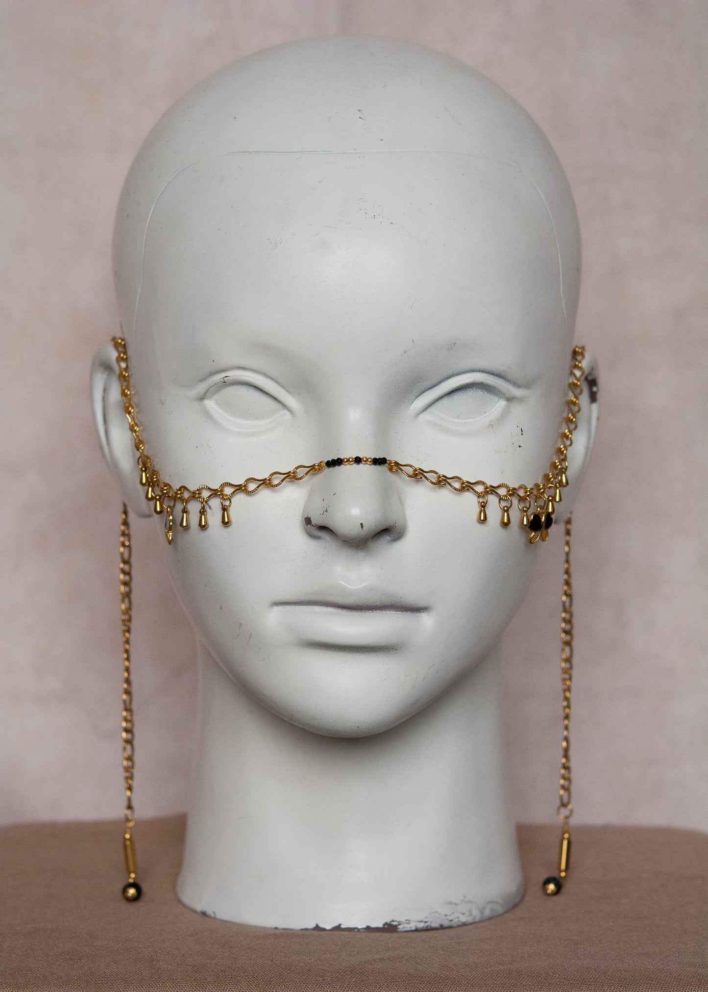 Bijou facial en chaîne d'acier inoxydable plaqué or avec breloques dorées et perles d’agate noire rayée. Accessoire symbolique, contrasté et mystique.