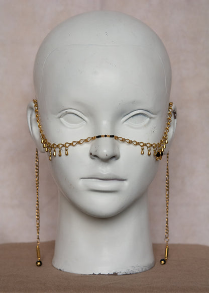 Bijou facial en chaîne d'acier inoxydable plaqué or avec breloques dorées et perles d’agate noire rayée. Accessoire symbolique, contrasté et mystique.