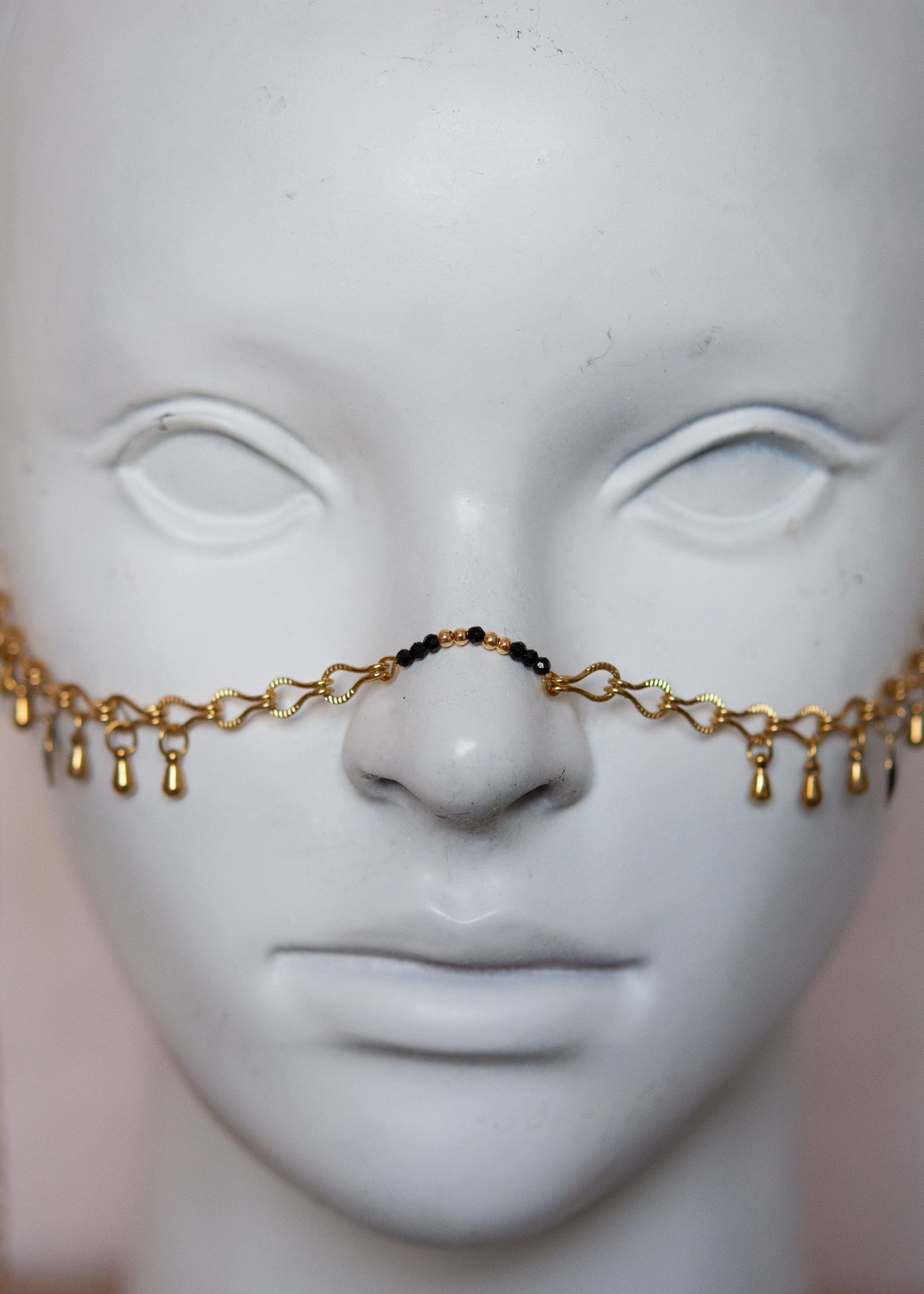 Bijou facial en chaîne d'acier inoxydable plaqué or avec breloques dorées et perles d’agate noire rayée. Accessoire symbolique, contrasté et mystique.