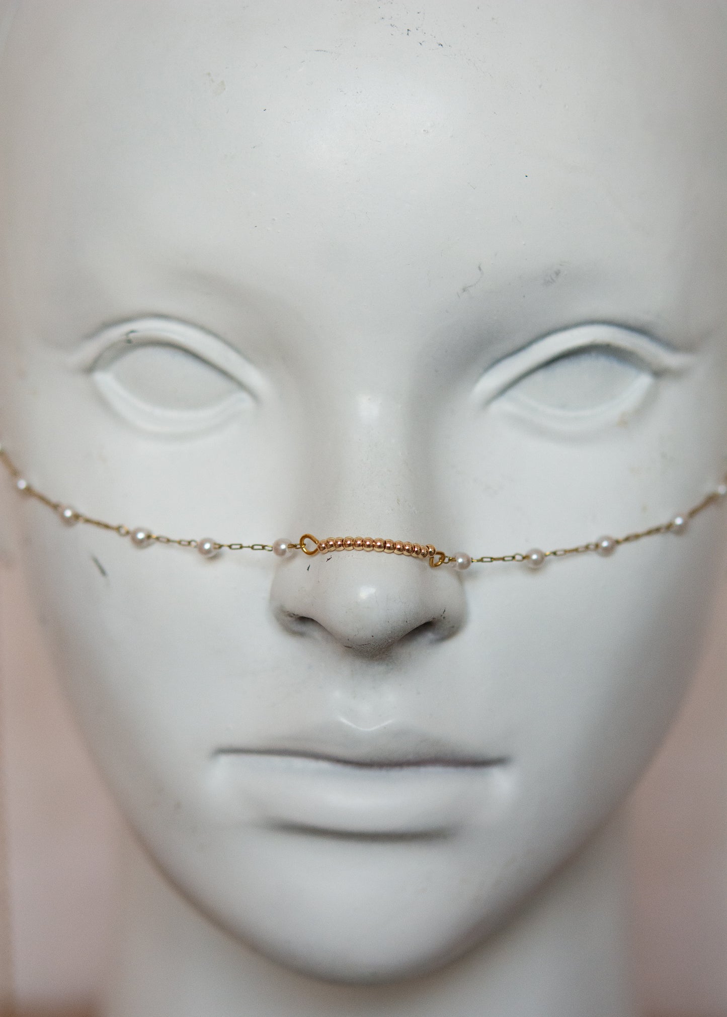 Bijou facial en chaîne d'acier inoxydable plaqué or avec perles synthétiques et plumes dorées. Accessoire léger et aérien, style boho, look festival.