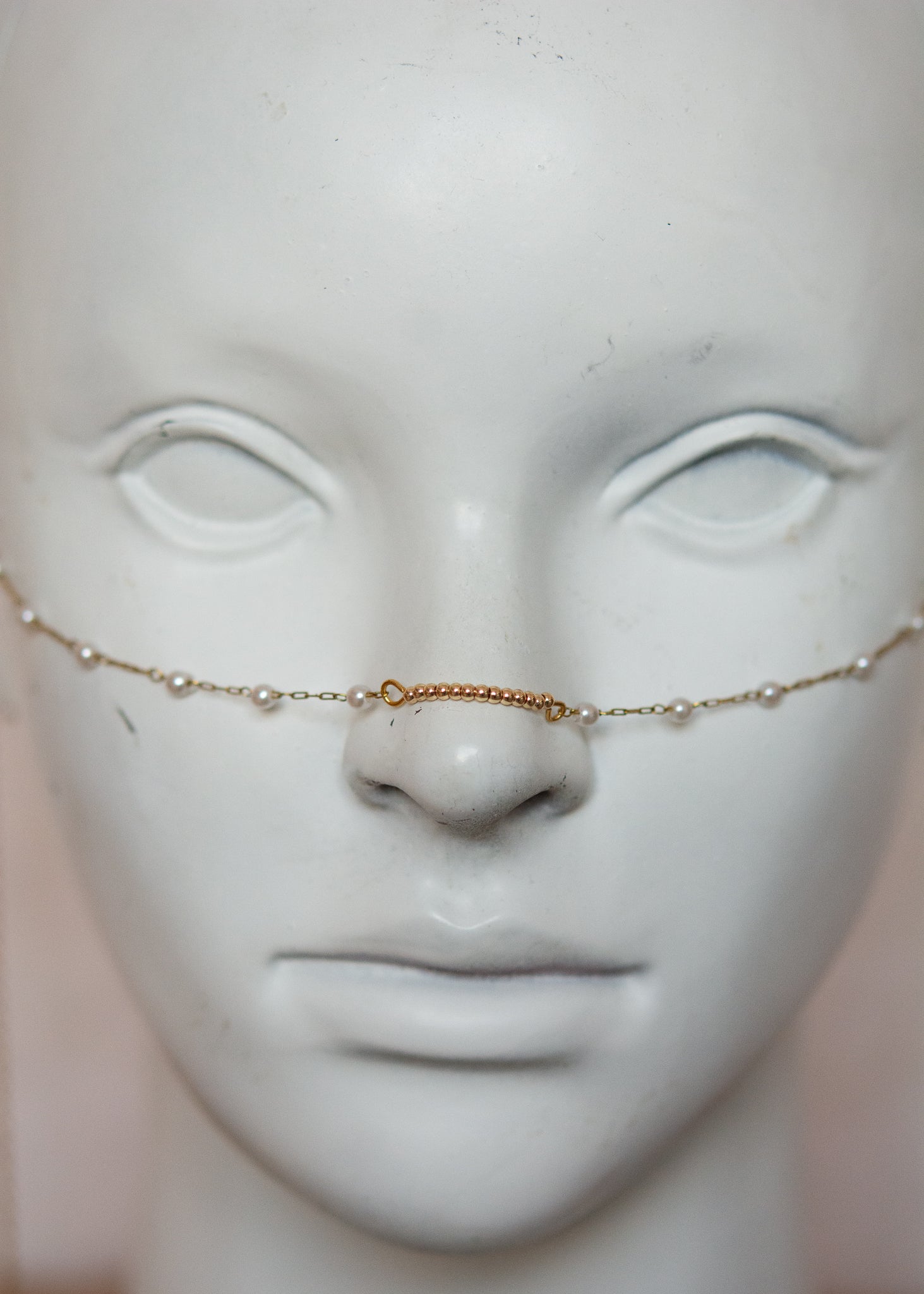 Bijou facial en chaîne d'acier inoxydable plaqué or avec perles synthétiques et plumes dorées. Accessoire léger et aérien, style boho, look festival.