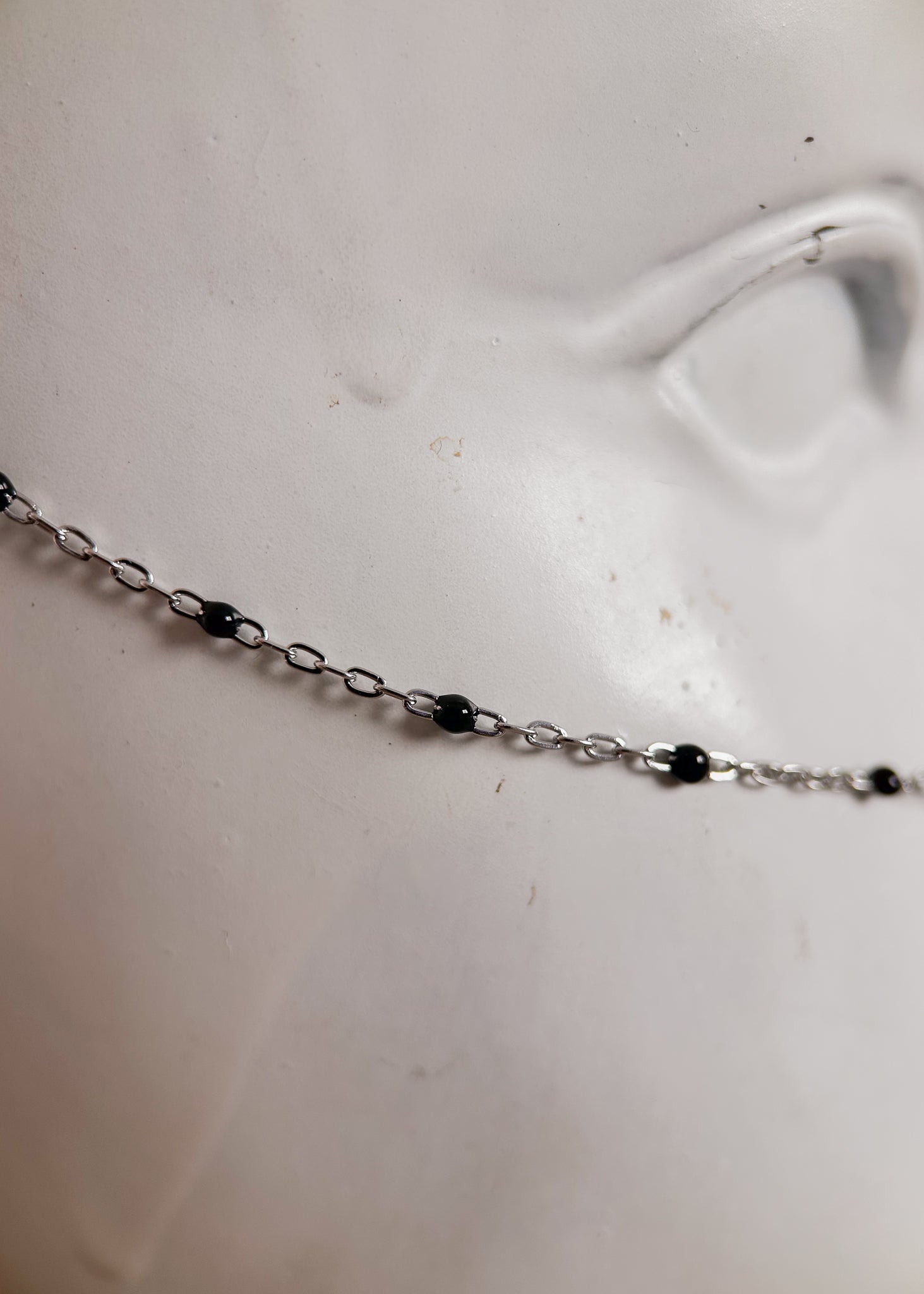 Bijou facial en chaîne fine avec perles d’émail noir et piques. Accessoire sombre et délicat pour look alternatif minimaliste.