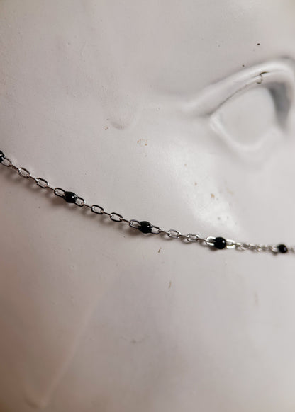 Bijou facial en chaîne fine avec perles d’émail noir et piques. Accessoire sombre et délicat pour look alternatif minimaliste.