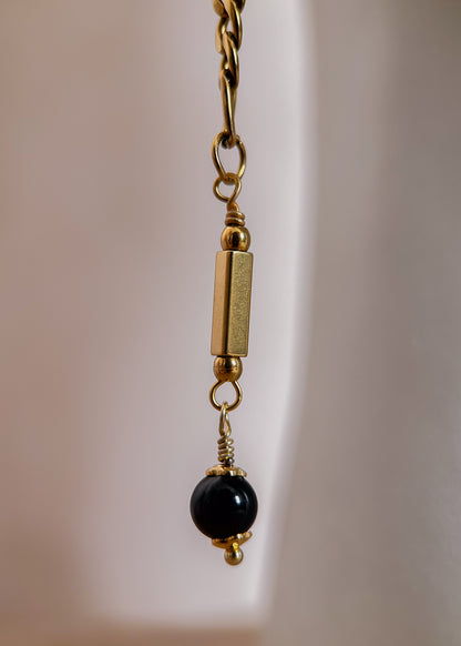 Bijou facial en chaîne d'acier inoxydable plaqué or avec breloques dorées et perles d’agate noire rayée. Accessoire symbolique, contrasté et mystique.