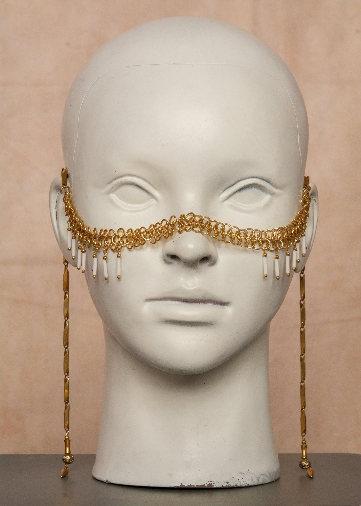 Chaîne de visage en acier inoxydable, assemblée à la main dans un motif de côte-de-maille avec perles tubes blanches et perles de lave dorées. Bijou mystique et guerrier, parfait pour les festivals et événements, ou pour ajouter une touche orientale à un look audacieux.