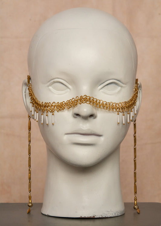 Chaîne de visage en acier inoxydable, assemblée à la main dans un motif de côte-de-maille avec perles tubes blanches et perles de lave dorées. Bijou mystique et guerrier, parfait pour les festivals et événements, ou pour ajouter une touche orientale à un look audacieux.