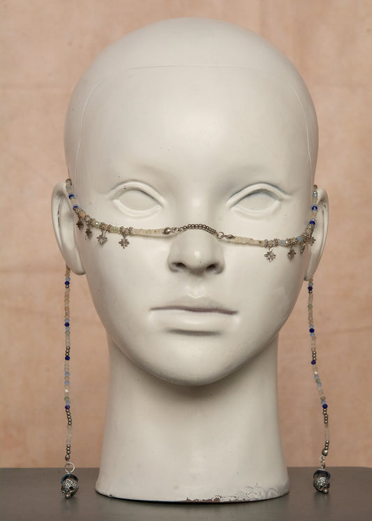Bijou facial artisanal combinant agate blanche, cristaux bleus et acier inoxydable. Accessoire céleste avec charmes étoiles et pierres de lune noires aux reflets holographiques transformées en lanternes orientales. Pièce unique apportant sérénité et équilibre, parfaite pour festivals nocturnes et événements mystiques.