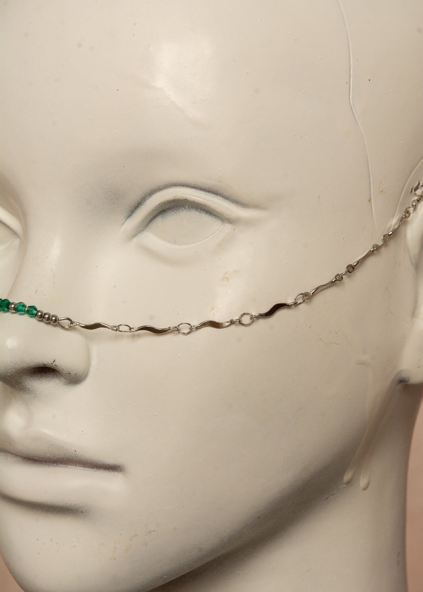 Chaîne de visage argentée en acier inoxydable, inspirée de la mythologie du serpent Basilic. Détails fluides et cristaux vert émeraude pour un look hypnotique et mystérieux, parfait pour les âmes audacieuses.