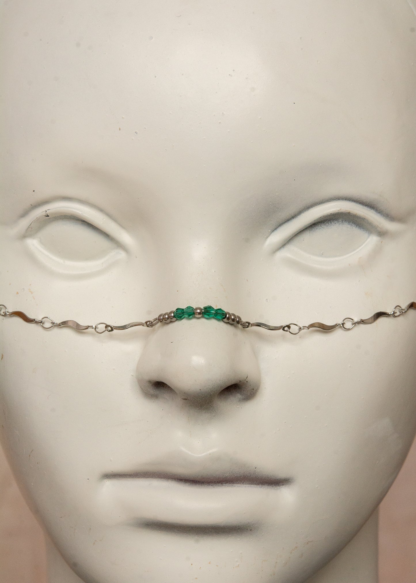 Chaîne de visage argentée en acier inoxydable, inspirée de la mythologie du serpent Basilic. Détails fluides et cristaux vert émeraude pour un look hypnotique et mystérieux, parfait pour les âmes audacieuses.