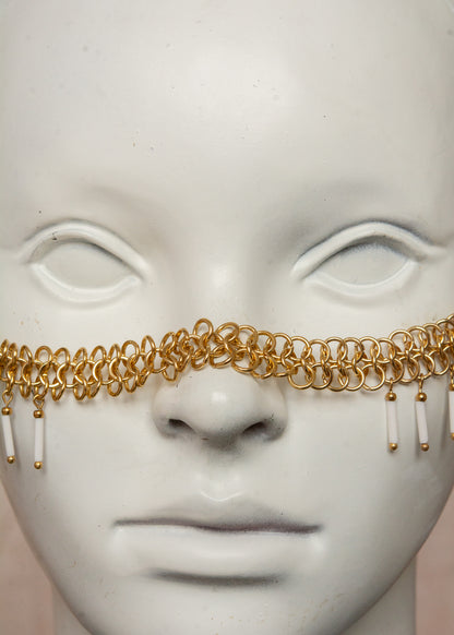Chaîne de visage en acier inoxydable, assemblée à la main dans un motif de côte-de-maille avec perles tubes blanches et perles de lave dorées. Bijou mystique et guerrier, parfait pour les festivals et événements, ou pour ajouter une touche orientale à un look audacieux.