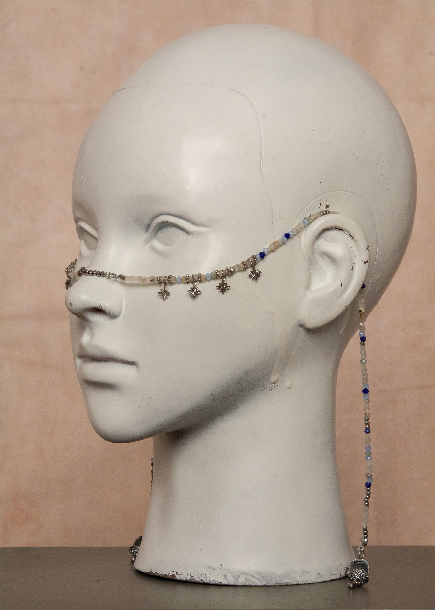 Bijou facial artisanal combinant agate blanche, cristaux bleus et acier inoxydable. Accessoire céleste avec charmes étoiles et pierres de lune noires aux reflets holographiques transformées en lanternes orientales. Pièce unique apportant sérénité et équilibre, parfaite pour festivals nocturnes et événements mystiques.