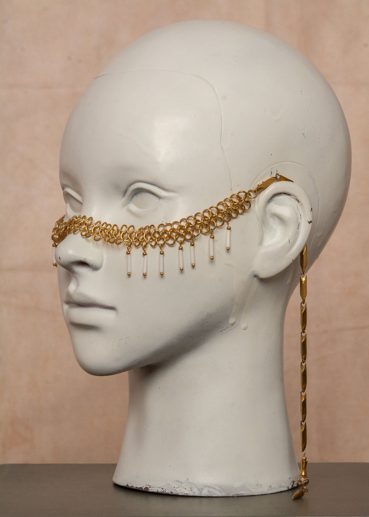 Chaîne de visage en acier inoxydable, assemblée à la main dans un motif de côte-de-maille avec perles tubes blanches et perles de lave dorées. Bijou mystique et guerrier, parfait pour les festivals et événements, ou pour ajouter une touche orientale à un look audacieux.