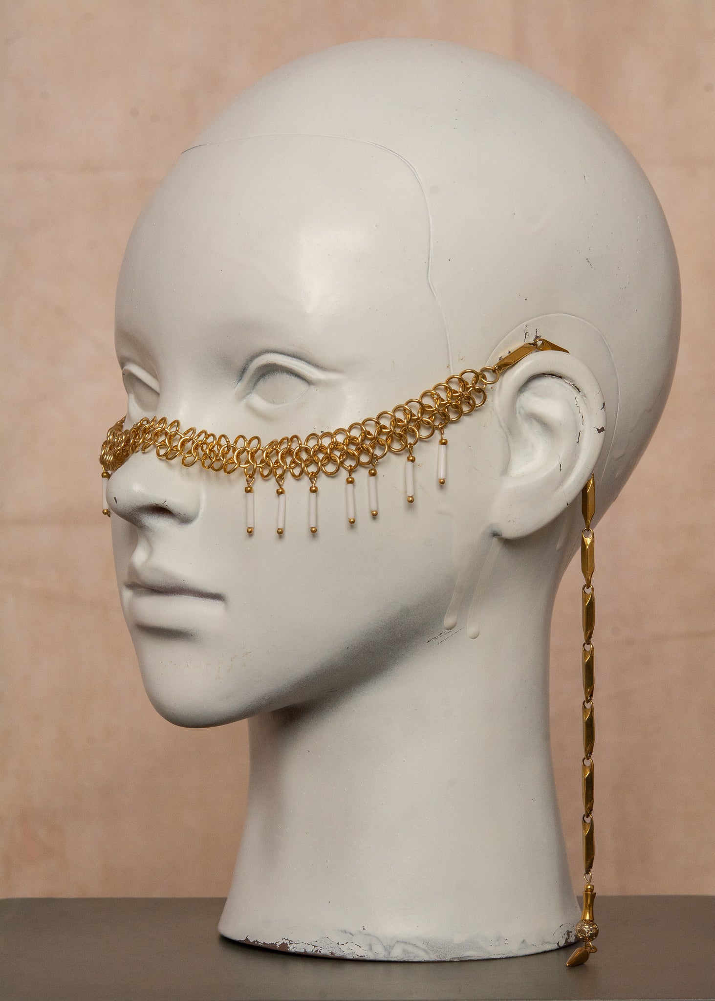 Chaîne de visage en acier inoxydable, assemblée à la main dans un motif de côte-de-maille avec perles tubes blanches et perles de lave dorées. Bijou mystique et guerrier, parfait pour les festivals et événements, ou pour ajouter une touche orientale à un look audacieux.